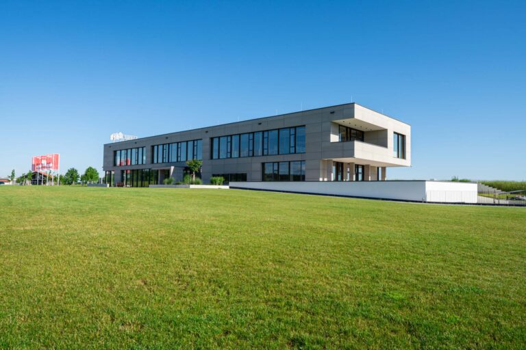 Modernes Bürogebäude in Niedereschach mit großen Fenstern, umgeben von einer weitläufigen grünen Rasenfläche und einem klaren blauen Himmel.