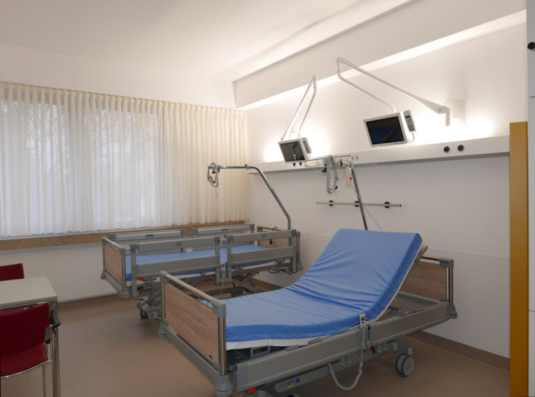 Zimmer im Klinikum Donaueschingen mit zwei Betten, medizinischen Geräten an der Wand und einem großen Fenster mit weißen Vorhängen.